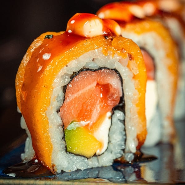 Close-up of SUSHARK's salmon, avocado, and cream cheese sushi roll, topped with orange sauce.