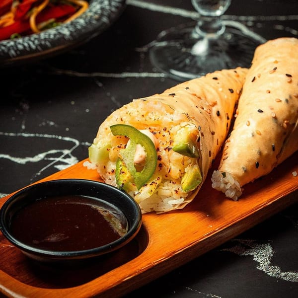 Two SUSHARK sushi hand rolls with avocado, jalapeño, and rice, served with dipping sauce.